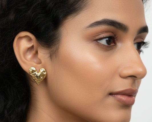 A close-up side profile of a woman wearing a textured, hammered gold heart-shaped stud earring.